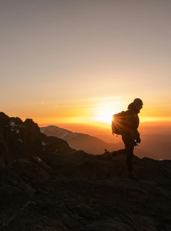silhouette of man standing on rock formation during sunset